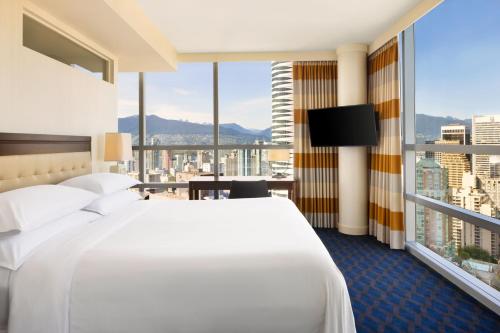 a hotel room with a white bed and a large window at Sheraton Vancouver Wall Centre in Vancouver