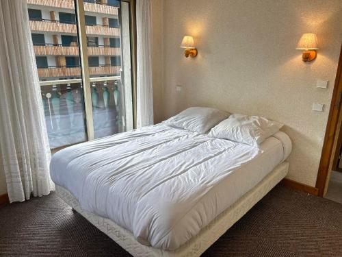 un lit dans une chambre avec une grande fenêtre dans l'établissement Les Gets: Appartement central 2 ch, balcon, au pied des pistes - FR-1-623-132, aux Gets