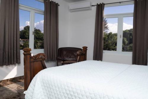 um quarto com uma cama, uma cadeira e janelas em Casa Blanca Mountain and Ocean Views em Rincon