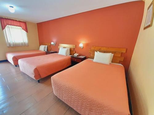 2 Betten in einem Hotelzimmer mit orangefarbenen Wänden in der Unterkunft Hotel y Restaurante Villa Esmeralda in Quetzaltenango