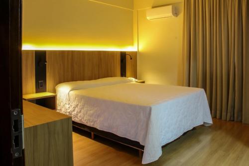 ein Schlafzimmer mit einem weißen Bett in einem Zimmer in der Unterkunft Hotel das Videiras in Videira