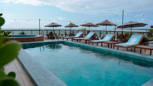 a swimming pool with lounge chairs and umbrellas at Atlântico Praia Hotel in João Pessoa