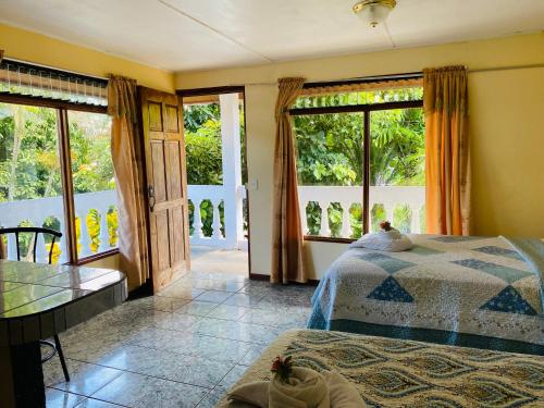 a bedroom with a bed and a table and windows at HOTEL QUEPOS PARAISO i in Quepos