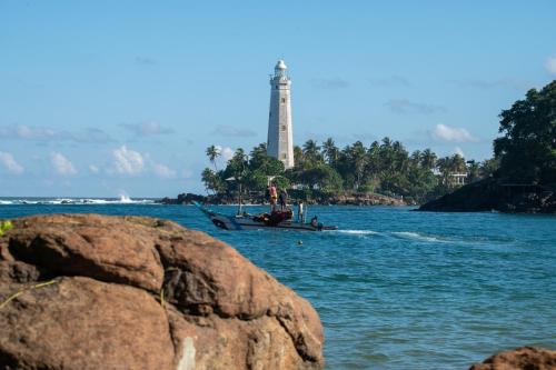 a boat in the water with a lighthouse in the background at Beacon By The Bay Villas and Suites by the Clarks in Matara