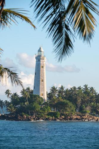 a lighthouse on an island in the ocean with palm trees at Beacon By The Bay Villas and Suites by the Clarks in Matara