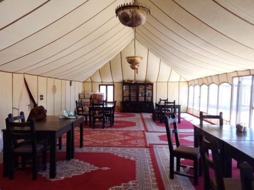 une chambre avec des tables et des chaises dans une tente dans l'établissement SAHARA WAVES CAMP, à Merzouga