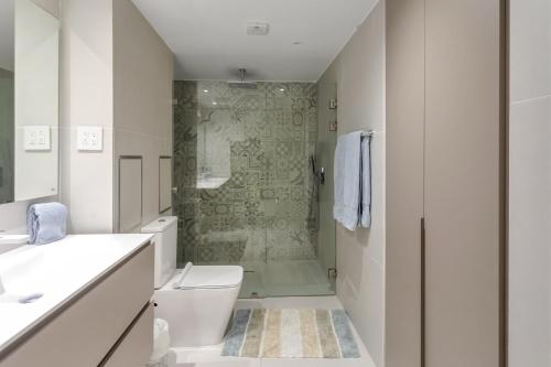 a white bathroom with a shower and a toilet at Maho Oceanfront Luxe: Modern and Spacious Condo in Maho Reef