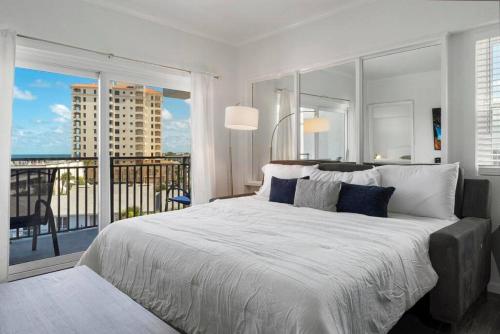 a white bedroom with a large bed and a balcony at Sandpiper Oceanfront 5F in Jacksonville Beach