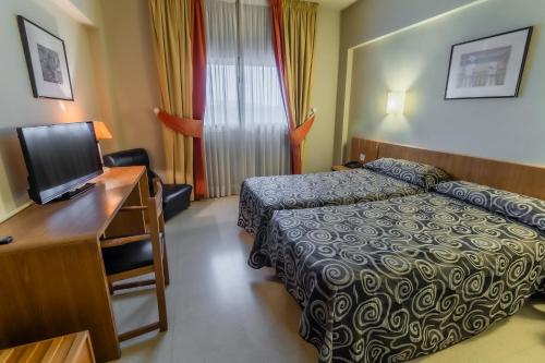 a hotel room with a bed and a desk with a television at Hotel Alhama in Cintruénigo