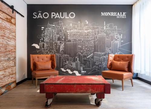 - deux chaises et une table basse devant une fresque murale représentant une ville dans l'établissement Monreale Lifestyle Higienópolis São Paulo, à São Paulo
