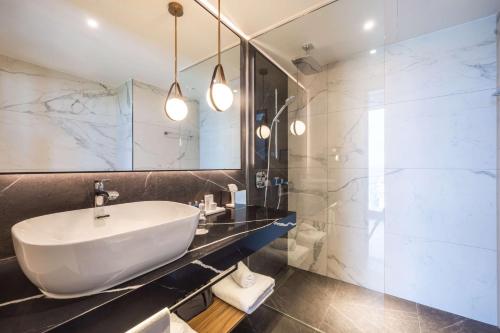 La salle de bains est pourvue d'un lavabo blanc et d'une douche. dans l'établissement Radisson Blu Hotel at Porsche Design Tower Stuttgart, à Stuttgart