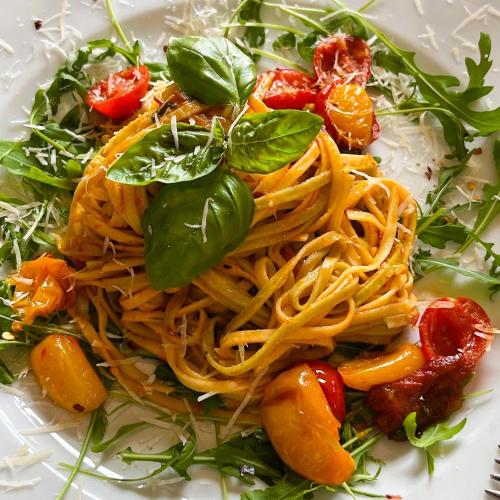 a plate of pasta with tomatoes and basil on it at PiranArt Boutique Hotel & More in Piran