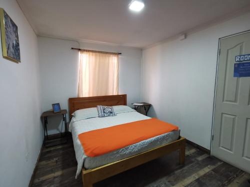 a small bedroom with a bed with an orange blanket at Hostel Punto Cavancha in Iquique
