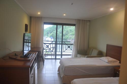 a hotel room with two beds and a desk and a balcony at Flat com vista para o mar! in Angra dos Reis
