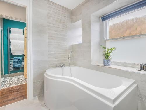 a white bathroom with a tub and a window at Pooley Bridge Apartment - Uk44955 in Pooley Bridge