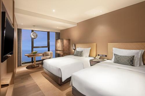 a hotel room with two beds and a television at Grand Bay Hotel Zhuhai in Zhuhai