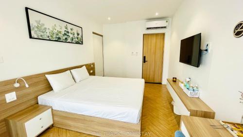 een slaapkamer met een wit bed en een televisie bij The Track Homestay in Cam Lâm