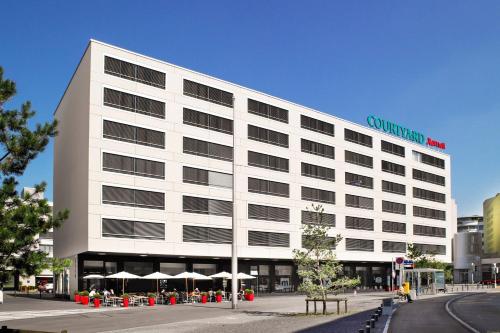 un grand bâtiment blanc avec des parasols en face de celui-ci dans l'établissement Courtyard by Marriott Zurich North, à Zurich