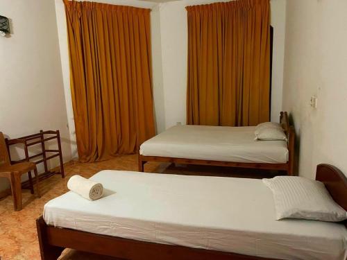 2 Betten in einem Zimmer mit orangefarbenen Vorhängen in der Unterkunft Mimosha Holiday Inn in Rambukkana