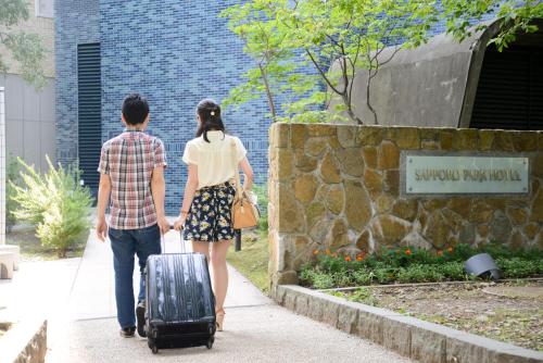 a man and a woman walking down a sidewalk with a suitcase at Sapporo Park Hotel in Sapporo