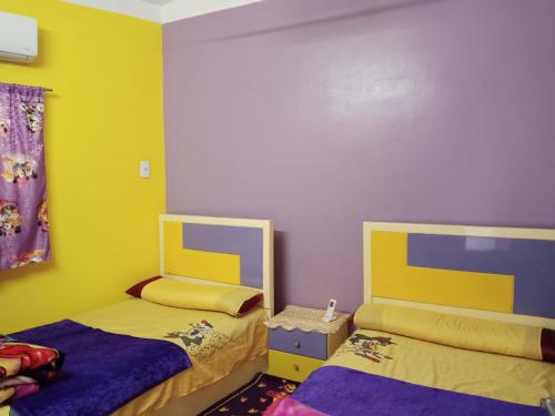duas camas num quarto com amarelo e roxo em Fekry home em Aswan