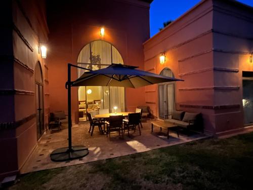 a patio with a table and an umbrella at night at Villa Magnolia - Amelkis Golf in Marrakech