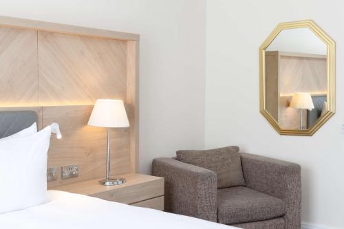 a bedroom with a bed and a chair and a mirror at Hilton Northampton Hotel in Northampton