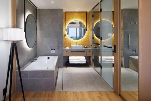 a bathroom with a tub and a sink and mirrors at Hilton Club The Beach Resort Sesoko in Motobu