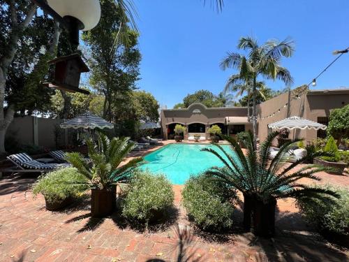 a swimming pool with two palm trees and a house at The Presidential at Forty 4 On Hoog Street in Polokwane