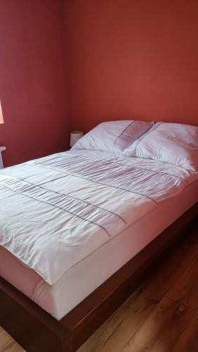 a bed with white sheets and a red wall at Apartamenty na 12 in Konstantynów Łódzki