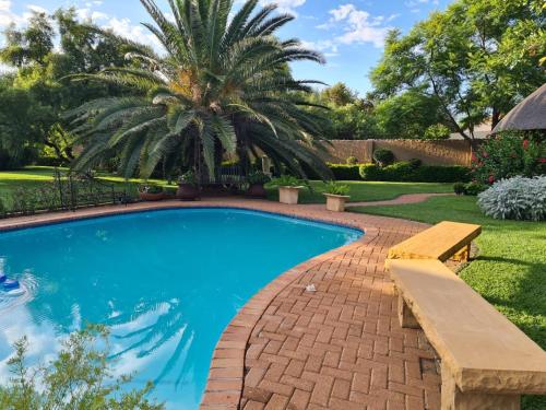 a swimming pool with a bench and a palm tree at Stone Town Guesthouse in Gaborone