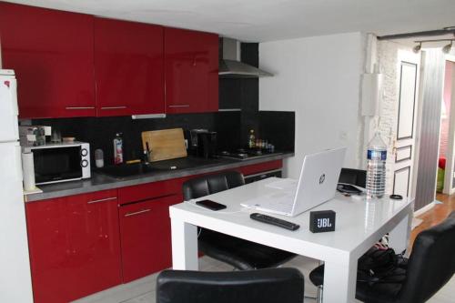 une cuisine avec des placards rouges et une table blanche avec un ordinateur portable dans l'établissement Appart'Hotel Saint-Omer, à Saint-Omer