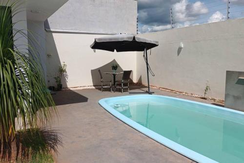 uma piscina com um guarda-sol e uma mesa com cadeiras em Chácara Horiental em Maringá