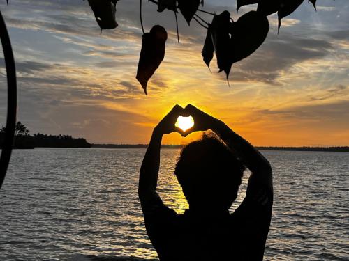 a person making a heart shape with the sunset in the background at SANTA MARIA HOSTEL MUNROE ISLAND in Munroe Island