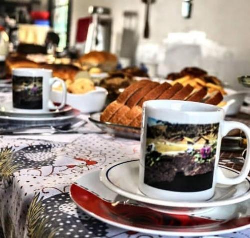 deux tasses à café et des soucoupes sur une table avec du pain dans l'établissement Pousada Laranjeiras Ecoturismo, à Bom Jardim da Serra