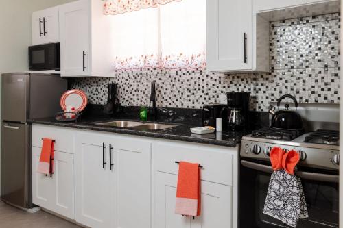 uma cozinha com armários brancos, um fogão e um lavatório em Thatch Garden Apartment em Long Bay Village
