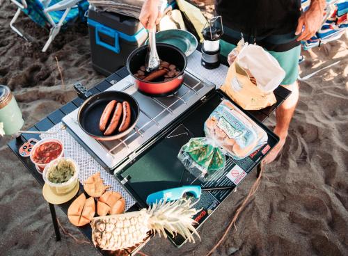 Un uomo che cucina cibo su una griglia sulla spiaggia di Zazu Campers a Kahului