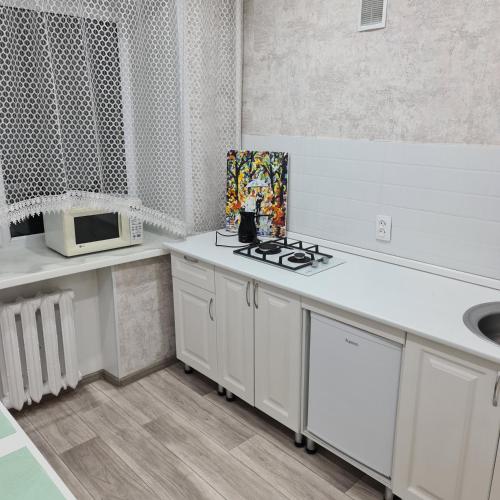 una cucina con mobili bianchi, un lavandino e un microonde di Дом77, проспект БухарЖырау a Karagandy