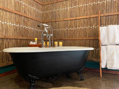 La salle de bains est pourvue d'une baignoire noire et de murs en bois. dans l'établissement umbila:Barra, à Inhambane