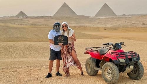 a man and a woman standing in the desert next to a quad bike at Shadow Pyramids Suites and Jacuzzi in Cairo
