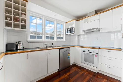 a white kitchen with wooden floors and white cabinets at Albert.T Home in Auckland