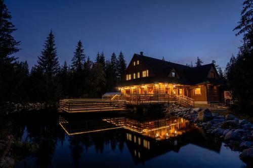 a log house with lights on the water at night at Rezort pri Jazere Podbanské in Vysoké Tatry