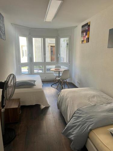 um quarto com 2 camas, uma mesa e janelas em Basel-Stadt Gundeldingen Zimmer 402, WC in the hallway, outside the room em Basileia