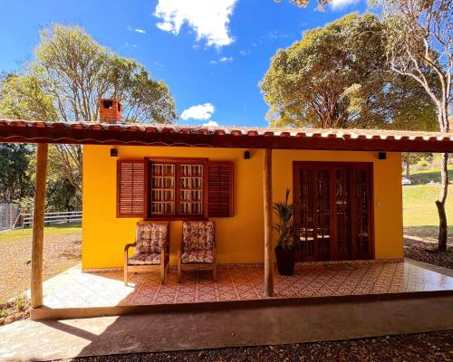a small yellow house with two chairs in front of it at Chalés Recanto da cachoeira in Monte Verde