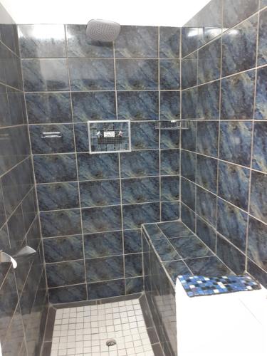 y baño con ducha de azulejos negros y aseo. en Rosies en George