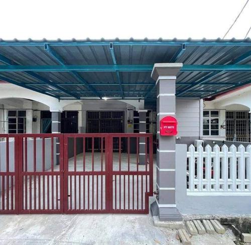a house with a red gate and a fence at SRI TEGUH HOMESTAY in Tanah Merah