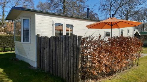 een klein huis met een oranje paraplu naast een hek bij Chalet Wad Mooi in Buren