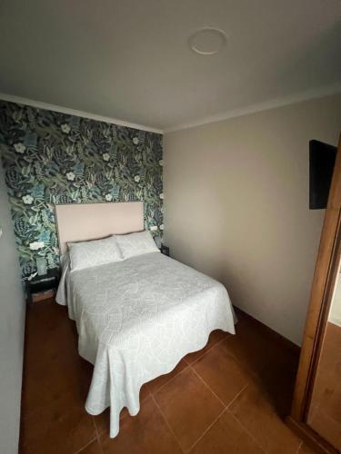 1 dormitorio con cama blanca y papel pintado con motivos florales en El Nido, en Pobra do Caramiñal