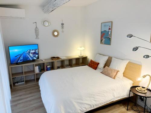 een slaapkamer met een wit bed en een flatscreen-tv bij Charmant studio climatisé à 200m de la plage in Mèze