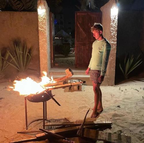 a boy standing in front of a grill with fire at Vilas na areia aparthotel in Sal Rei